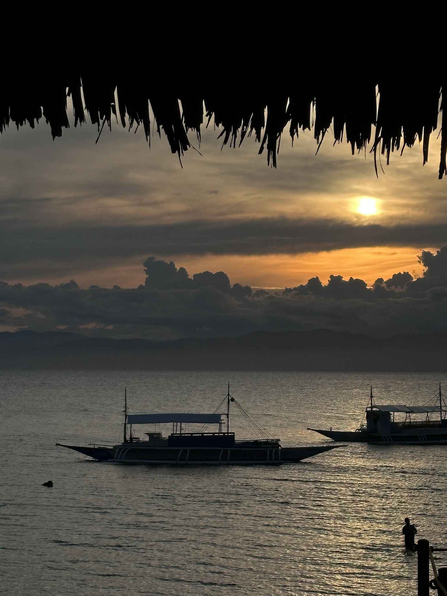 Sunset over the sea with silhouetted bangka boats under nipa roof